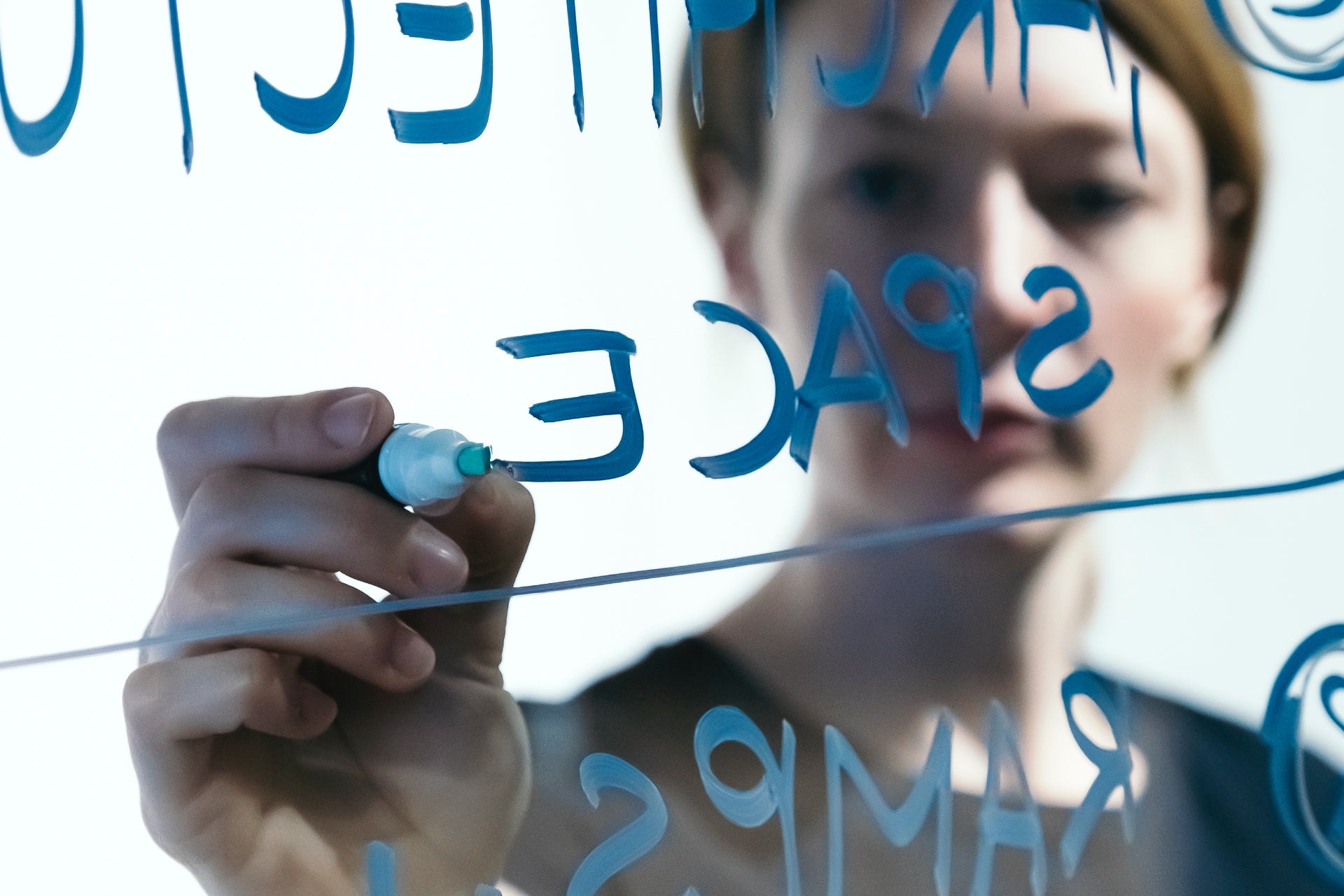 Eine Person schreibt mit einem blauen Marker das Wort Space auf ein Glasboard.